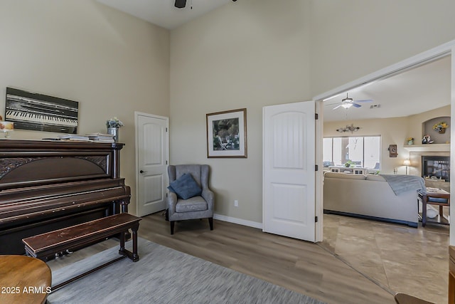 living area with baseboards, a glass covered fireplace, ceiling fan, wood finished floors, and a high ceiling