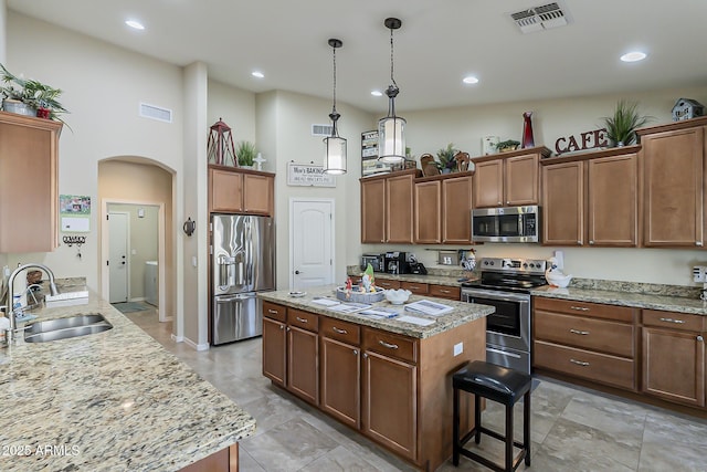 kitchen with arched walkways, a kitchen island, a sink, visible vents, and appliances with stainless steel finishes