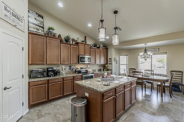 kitchen featuring a toaster, decorative light fixtures, stainless steel appliances, a kitchen island, and light stone countertops