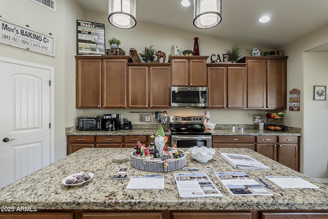 kitchen with light stone counters, a center island, lofted ceiling, visible vents, and appliances with stainless steel finishes