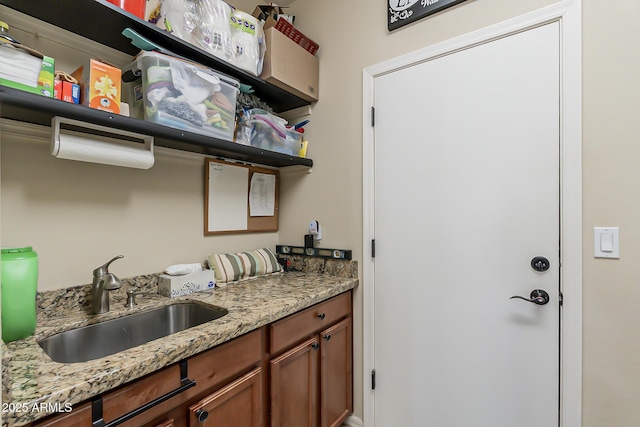 kitchen featuring light stone countertops, brown cabinets, a sink, and open shelves