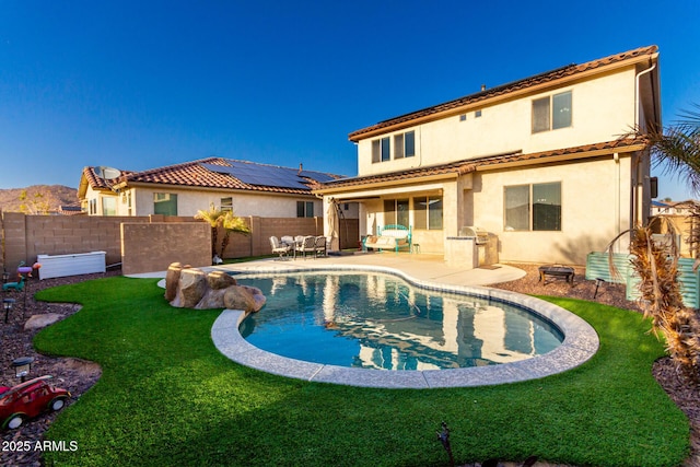 rear view of property featuring a fenced in pool, a lawn, a patio area, and solar panels