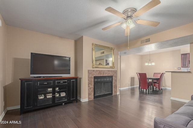 living room featuring a textured ceiling, ceiling fan with notable chandelier, a tiled fireplace, and dark hardwood / wood-style floors