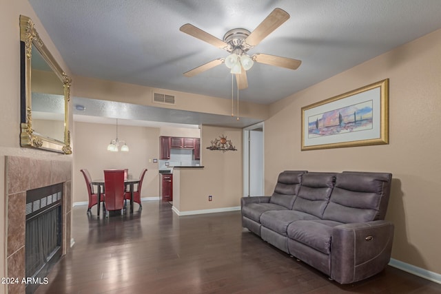 living room with a textured ceiling, ceiling fan with notable chandelier, a tiled fireplace, and dark hardwood / wood-style floors