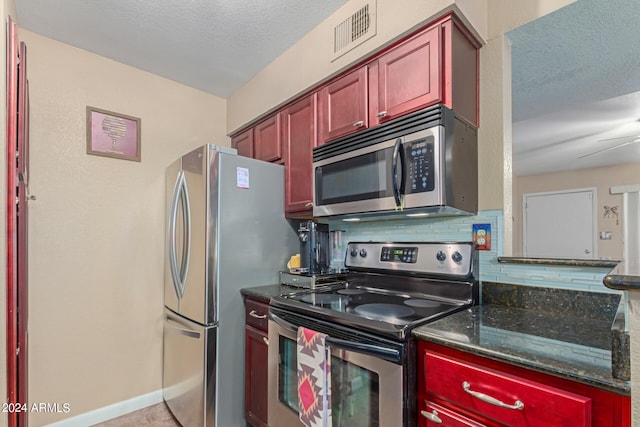 kitchen with a textured ceiling, decorative backsplash, appliances with stainless steel finishes, dark stone countertops, and ceiling fan