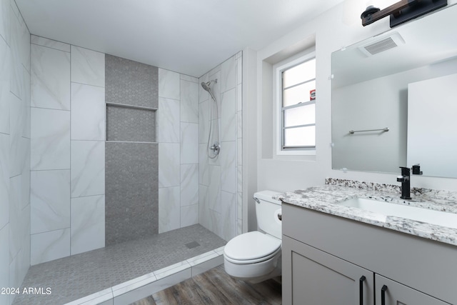 bathroom featuring wood-type flooring, vanity, a tile shower, and toilet