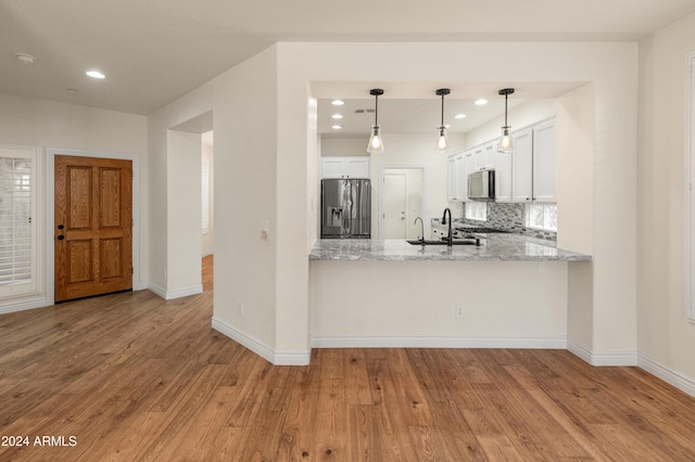 kitchen featuring kitchen peninsula, light hardwood / wood-style flooring, appliances with stainless steel finishes, decorative light fixtures, and white cabinetry