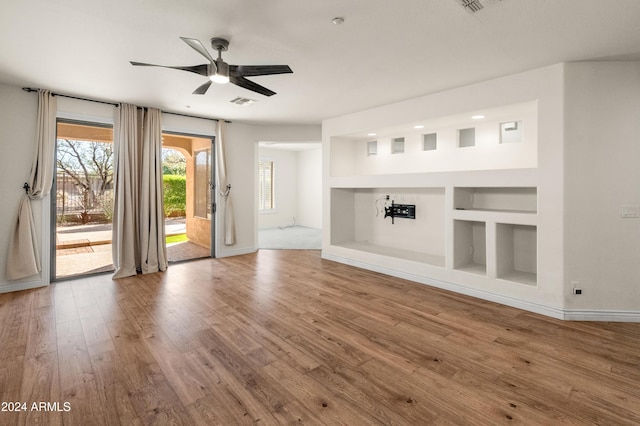 unfurnished living room with built in shelves, hardwood / wood-style flooring, and ceiling fan