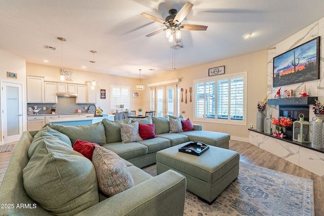 living room featuring sink, hardwood / wood-style flooring, a large fireplace, and ceiling fan