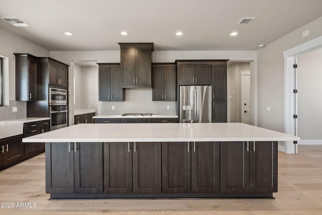 kitchen with a spacious island, dark brown cabinets, appliances with stainless steel finishes, and light hardwood / wood-style flooring