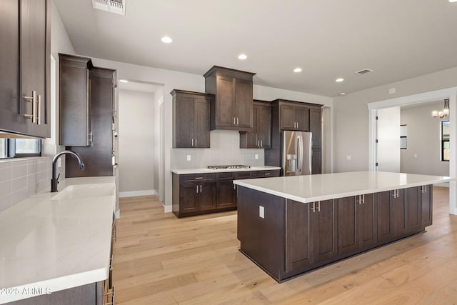 kitchen with sink, light hardwood / wood-style flooring, appliances with stainless steel finishes, tasteful backsplash, and a kitchen island