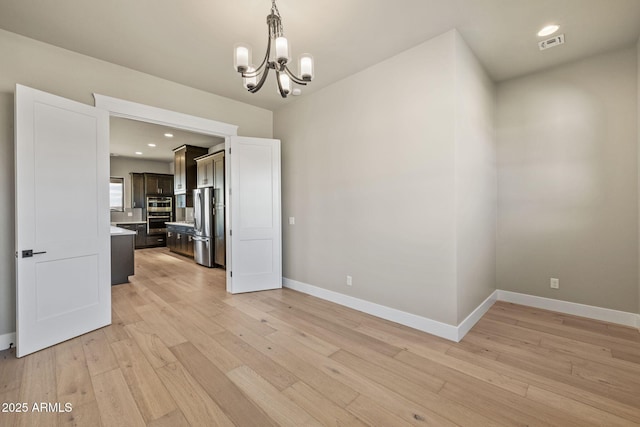 empty room with light hardwood / wood-style flooring and a notable chandelier