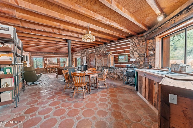 dining space with wood ceiling, beam ceiling, sink, and a wood stove