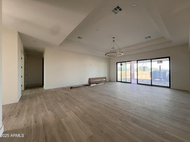 empty room with a raised ceiling, baseboards, visible vents, and light wood-type flooring