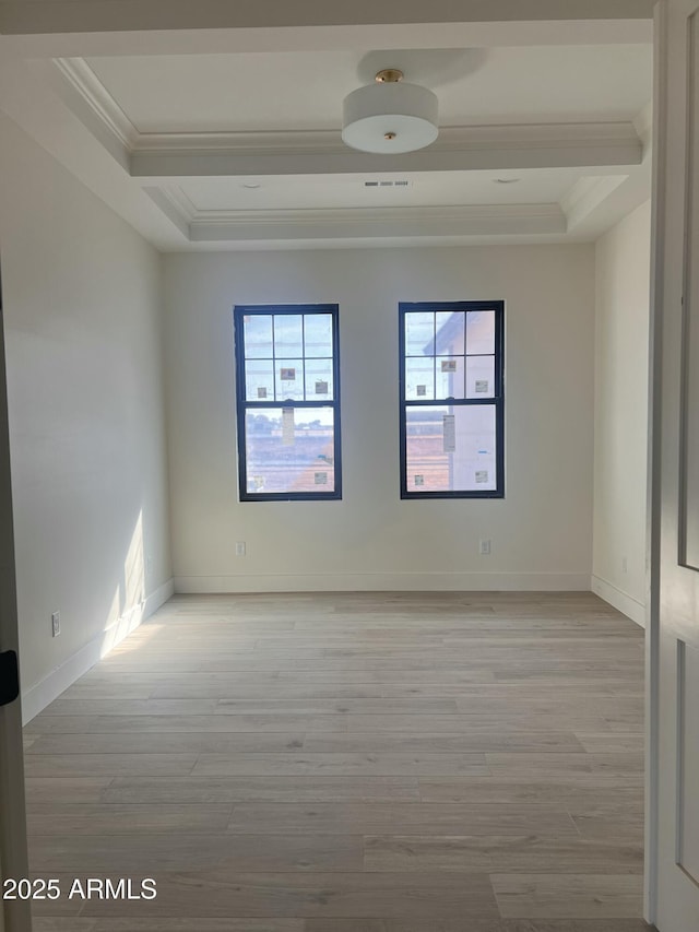 spare room featuring baseboards, a raised ceiling, ornamental molding, and light wood finished floors