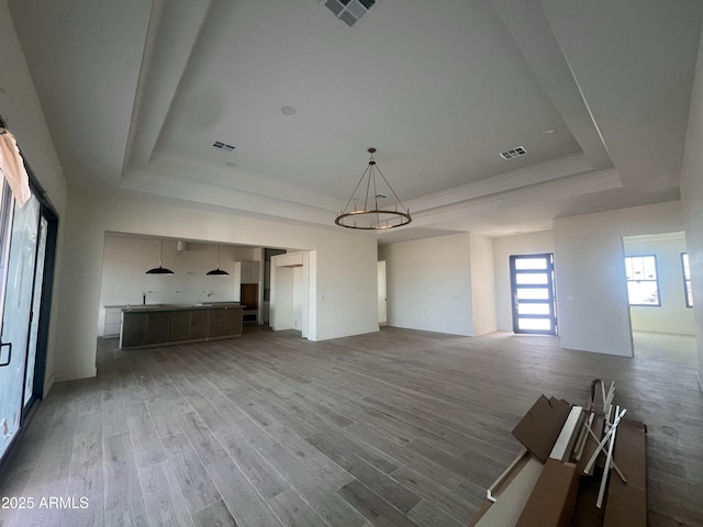 unfurnished living room with visible vents, ornamental molding, a tray ceiling, and wood finished floors