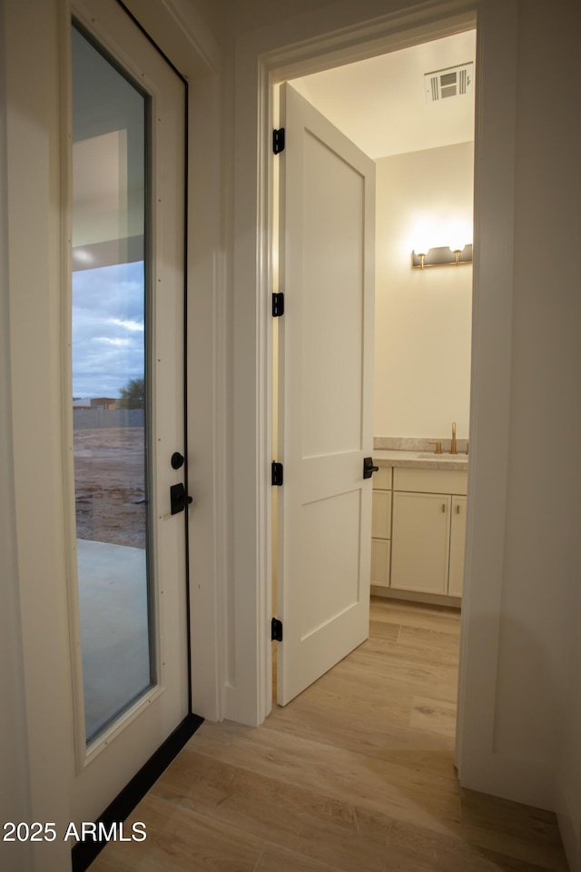 hallway with visible vents, light wood-type flooring, and a sink