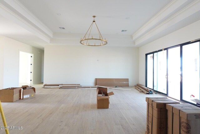 unfurnished living room featuring an inviting chandelier, a tray ceiling, visible vents, and light wood finished floors