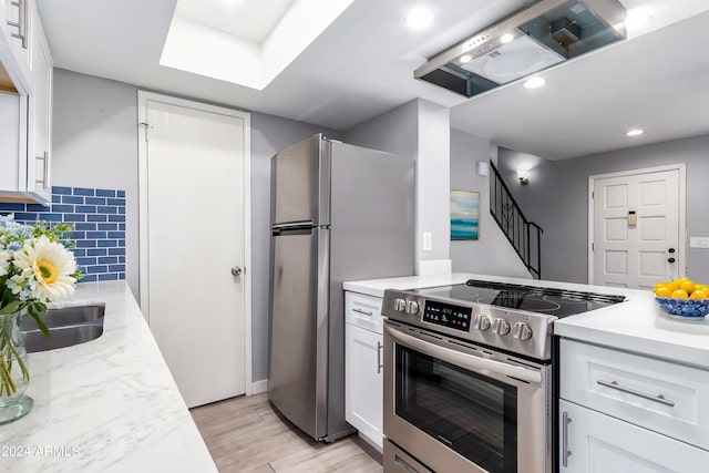 kitchen with white cabinets, backsplash, light hardwood / wood-style flooring, appliances with stainless steel finishes, and sink