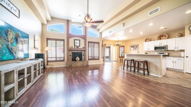 unfurnished living room featuring baseboards, visible vents, wood finished floors, a fireplace, and ceiling fan with notable chandelier