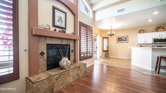 living area featuring visible vents, an inviting chandelier, wood finished floors, a tile fireplace, and baseboards