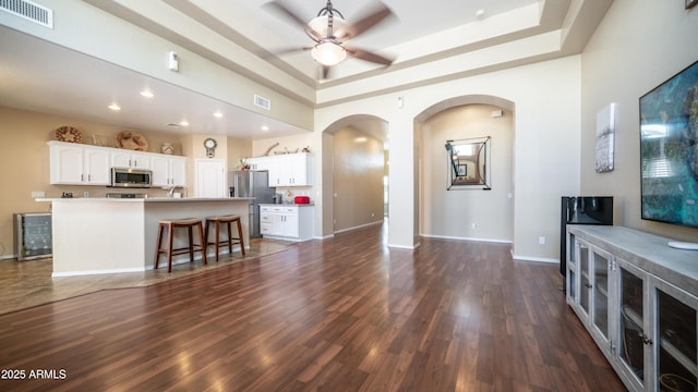 living room featuring arched walkways, dark wood-style flooring, a raised ceiling, visible vents, and baseboards