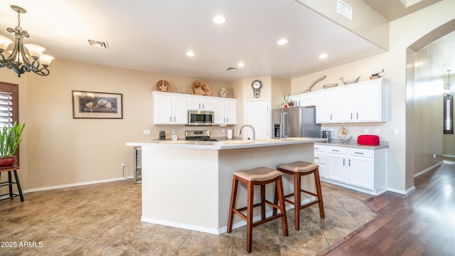 kitchen featuring stainless steel appliances, white cabinets, light countertops, and a center island with sink