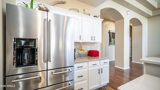 kitchen with high end refrigerator, arched walkways, white cabinets, and light countertops