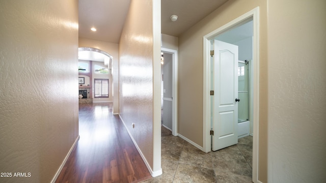 hall with baseboards, arched walkways, and a textured wall