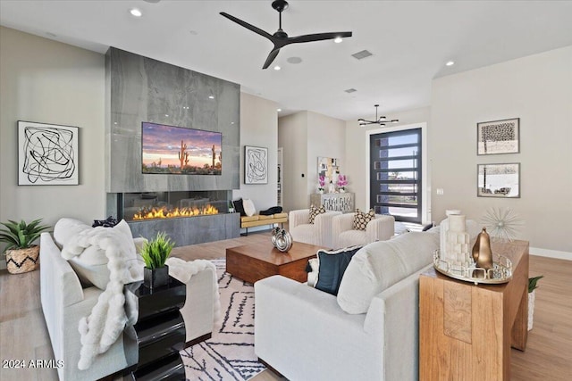 living room featuring a large fireplace, light hardwood / wood-style flooring, and ceiling fan