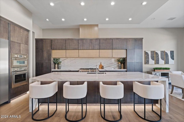 kitchen with a spacious island, decorative backsplash, light wood-type flooring, and a kitchen bar