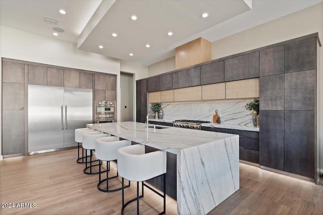 kitchen with appliances with stainless steel finishes, sink, light wood-type flooring, a large island, and decorative backsplash