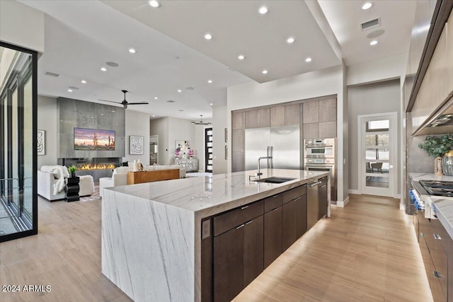 kitchen featuring a spacious island, a tiled fireplace, sink, and light hardwood / wood-style floors