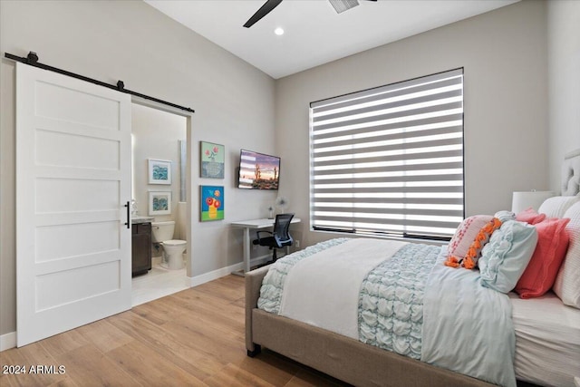 bedroom featuring connected bathroom, light hardwood / wood-style flooring, a barn door, and ceiling fan