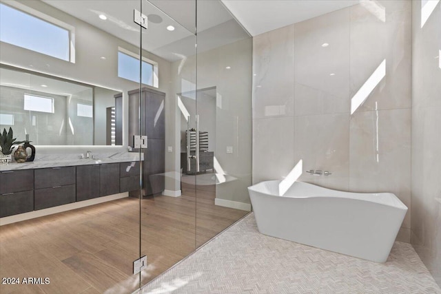 bathroom with a high ceiling, vanity, hardwood / wood-style floors, tile walls, and shower with separate bathtub