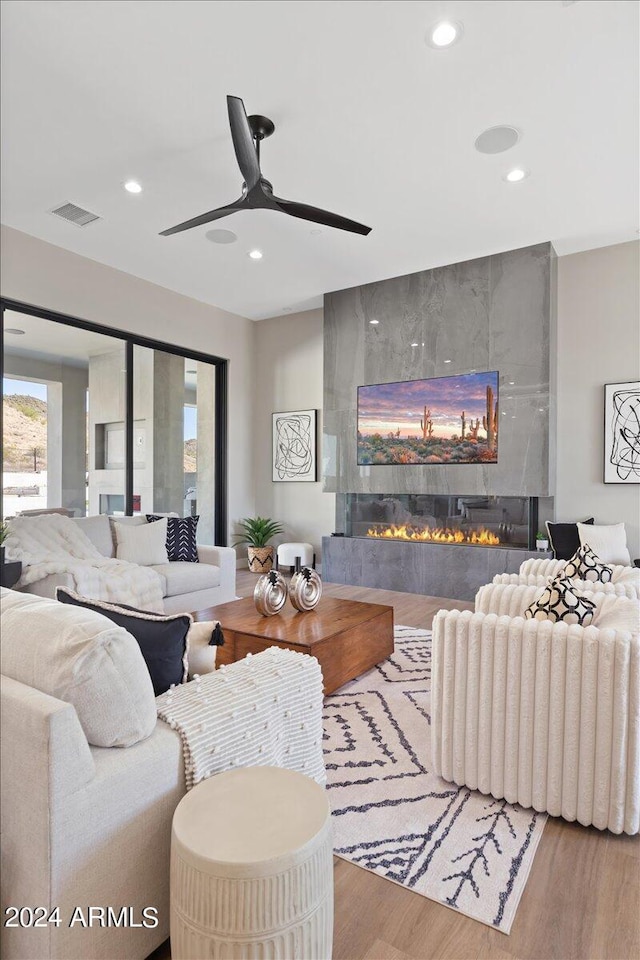 living room with ceiling fan, wood-type flooring, and a tile fireplace