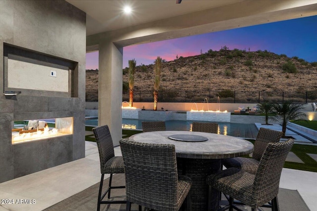 patio terrace at dusk featuring pool water feature and an outdoor fire pit