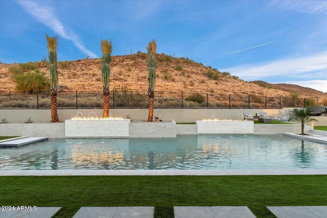 view of swimming pool with a mountain view, pool water feature, and a yard