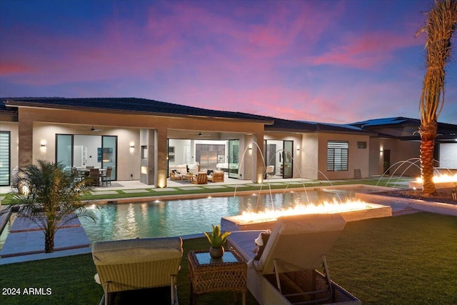 pool at dusk with a patio area, pool water feature, a yard, and a fire pit