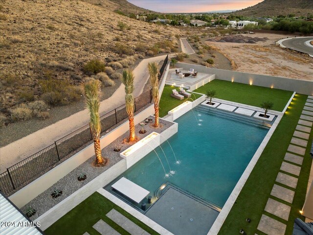 pool at dusk featuring a patio and pool water feature