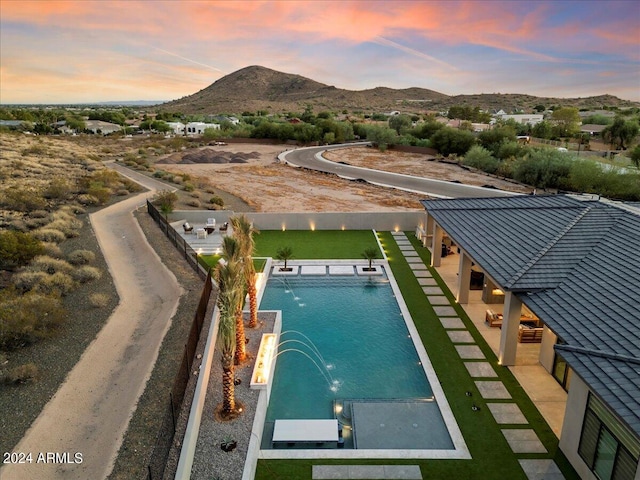 pool at dusk with a patio, a mountain view, and pool water feature