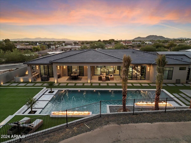 pool at dusk with a yard, pool water feature, a mountain view, and a patio