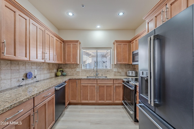 kitchen featuring sink, decorative backsplash, light stone countertops, light wood-type flooring, and stainless steel appliances