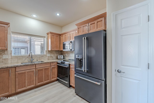 kitchen with sink, tasteful backsplash, light stone counters, light hardwood / wood-style floors, and appliances with stainless steel finishes