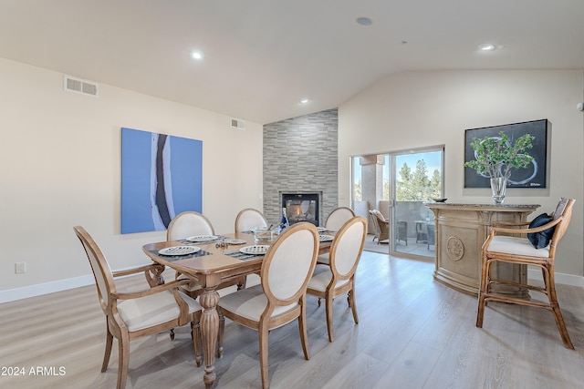 dining room featuring a large fireplace, light hardwood / wood-style flooring, and vaulted ceiling