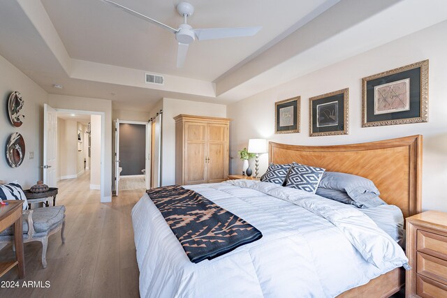 bedroom with a raised ceiling, ceiling fan, and light hardwood / wood-style flooring