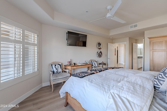 bedroom featuring a tray ceiling, connected bathroom, ceiling fan, and light hardwood / wood-style flooring