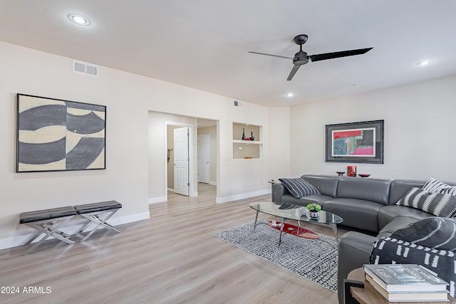 living room featuring built in shelves, ceiling fan, and light hardwood / wood-style flooring