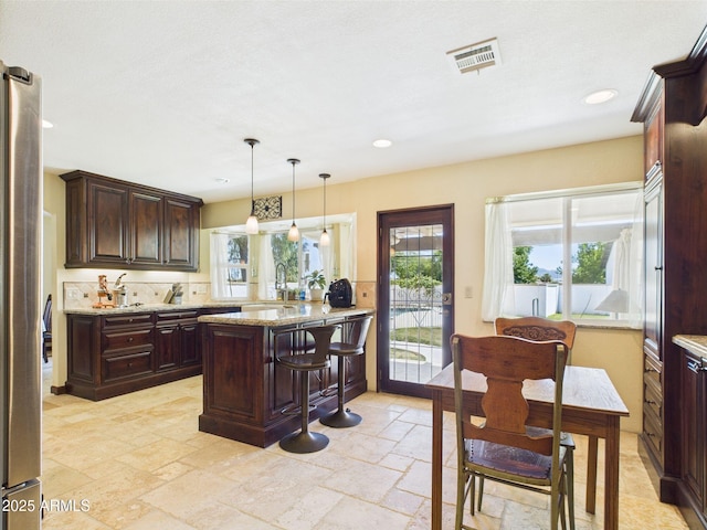 kitchen featuring a peninsula, a sink, stone tile flooring, freestanding refrigerator, and dark brown cabinetry