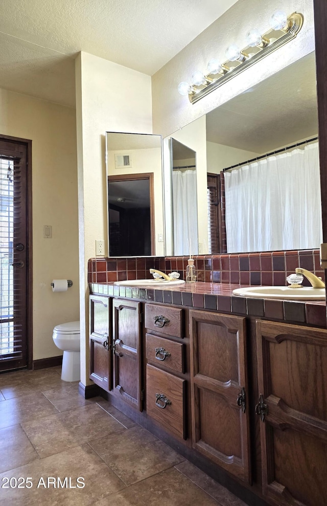 bathroom with toilet, decorative backsplash, vanity, and baseboards